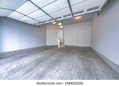 Empty Interior Of A White Garage With No People Or Items. There Is A Clean Gray Concrete Floor With White Walls. The Sliding Door Is Open.