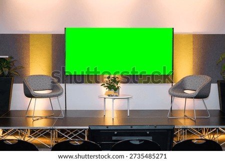 Empty interview stage featuring large green screen chroma key backdrop with modern lounge chairs and professional lighting