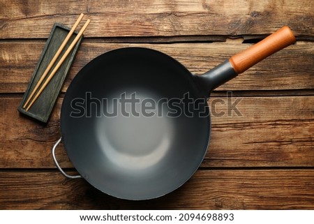 Empty iron wok and chopsticks on wooden table, flat lay