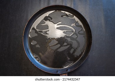 An empty kitchen pan against a dark background. Round metal frying pan with cooking oil. Top view.