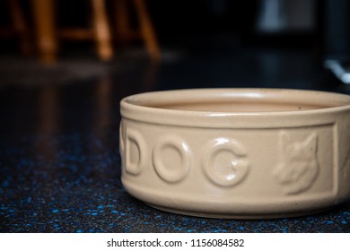 An Empty Large Ceramic Dog Food Bowl On A Dark Kitchen Floor