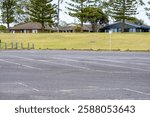 Empty and large outdoor parking lot with multiple open-air parking spaces and a few houses in the background. Copy space for design.