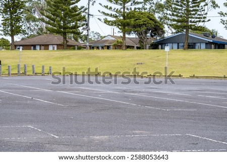 Empty and large outdoor parking lot with multiple open-air parking spaces and a few houses in the background. Copy space for design.