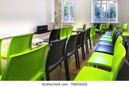 Empty lecture hall - small class room with green and black plastic chairs and big bright windows. Comfort space for learning.