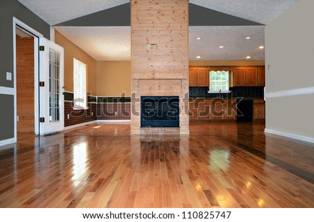 An empty living area with a fireplace.  Behind it is the dining and kitchen area.