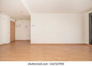 Empty Living Room Of An Apartment With Wooden Floors, White Aluminum Radiators, Freshly Painted Walls In Plain White Color And Access Door In Beech Wood Color