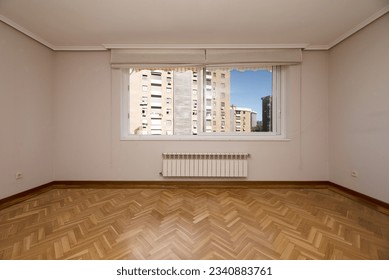 Empty living room with French oak parquet flooring arranged in a herringbone pattern, white aluminum windows with shutters and heating below and views of buildings outside