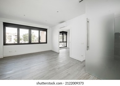 Empty Living Room In A Loft With Large Black Aluminum Windows With Gray Wood-like Ceramic Floors And Opaque Glass Sliding Door