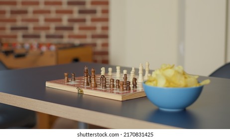 Empty Living Room Table With Chess Board Game And Bowl Of Chips, No People In Apartment Used To Meet And Have Fun With Strategic Activity. Nobody In Space With Checkmate Play. Close Up.