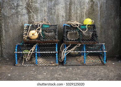 Empty lobster pots stacked against a sea harbour wall. Isolated lobster pots made from a frame with netting stretched over it.  Yellow floats attached with rope waiting to be used.