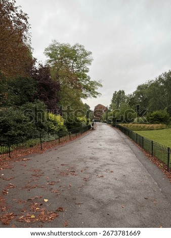 Empty London park path surrounded by green foliage on a dark cloudy autumn day. 