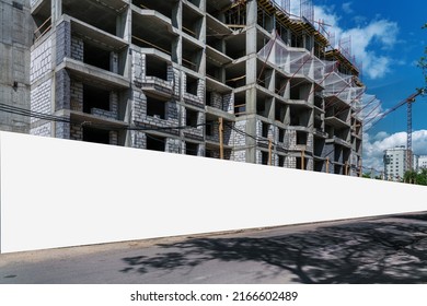 Empty long hoarding with white mockup space on construction site against grey wall of unfinished building.