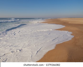 Empty long wide beach, yellow sand, Nazare; big portugal curling wave; power energy of nature; beautiful atlantic ocean background; wave for surfing camp; sport leisure activity; splashing wave crest