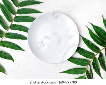 Empty Marble Plate With Tropical Leaves On White Textured Background. Minimalist Summer Table Setting. Top View.