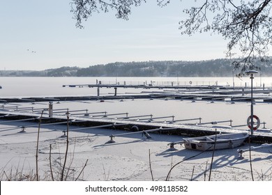 Empty marina. Winter view of mooring with only one boat beside lifebuoy. Beautiful landscape with row of free piers on frozen lake. Bright sun over lake covered with ice and snow. Sunny day. Your text