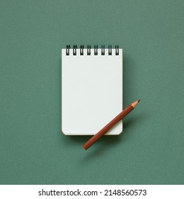 Empty memo note pad with brown pencil on green background. top view, copy space