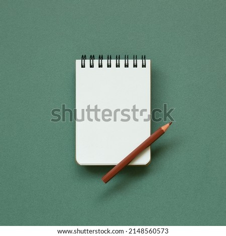 Empty memo note pad with brown pencil on green background. top view, copy space