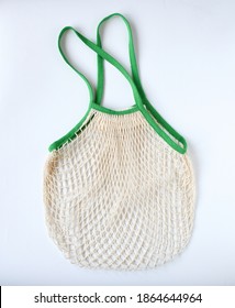 Empty Mesh Shopping Bag, White Net Cotton String With Green Holding Border On White Background. Tote Bag Contain Vegetable Or Fruit, Reuseable And Washable, Eco Market Bag Concept.