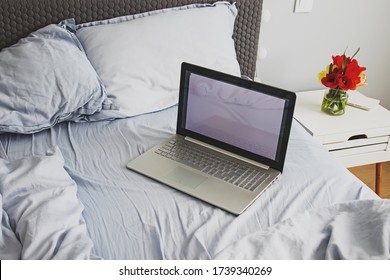 Empty Messy Grey Bed With Laptop In Minimalist Bedroom With Flowers On The Night Stand. Modern Lifestyle Concept, Work From Home