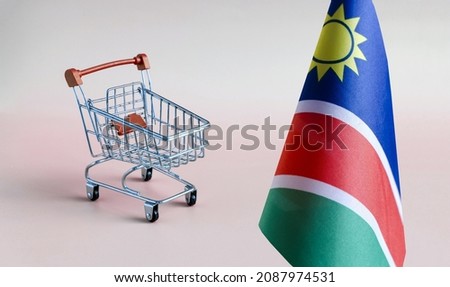 An empty metal shopping basket and the flag of the Republic of Namibia on a light background - the concept of consumption and consumer basket.
