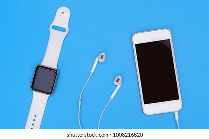 Empty Mobile Phone With Smartwatch Gadgets And Earphone On Blue Top View Flat Lay For Hi Tech Gadgets And Sport Technology Concept With Blank Screen For Application Mock Up