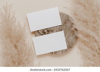 Empty mockup business card on marble stand and pampas grass. Aesthetic paper card template for business, invitation, logo, blog, design and social media, simple bohemian style, top view.