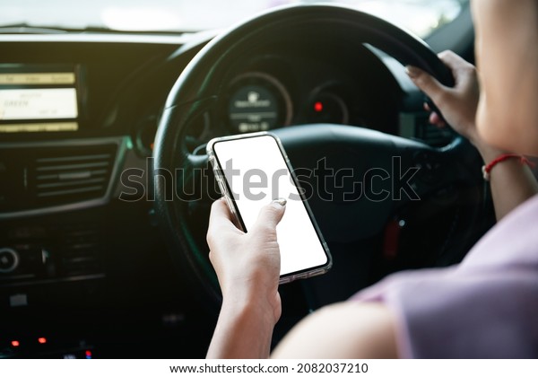 Empty\
mockup smartphone screen with clipping path. Asian young\
businesswoman using a smartphone while driving a car, careless\
woman driver using a phone while driving a\
car.