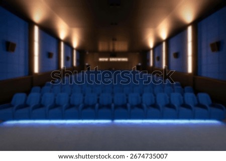 An empty, modern cinema auditorium features rows of plush blue seats illuminated by subtle blue floor lighting. The 