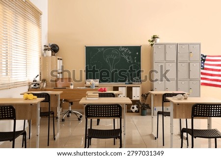 Empty modern classroom interior with desks, chairs, chalkboard, lockers, and american flag for education and learning