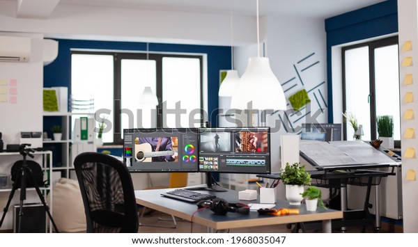Empty modern creative agency office with dual\
monitors setup with processing video film montage. Video editing\
start up studio company with no people in it and post production\
software on pc displays