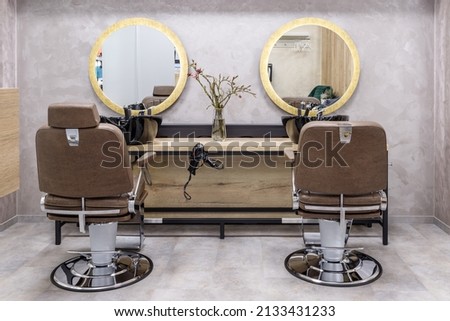 Empty modern interior of hair salon in golden and grey color. Luxury men's seats with a table sink  for washing hair and round mirror in a barber shop