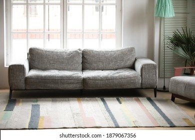 Empty Modern Living Room With Comfortable Grey Couch And Armchair, Colorful Carpet On Floor, Green House Plant, Large Window Behind Gray Sofa, Mortgage, Cozy Furniture In New First Apartment