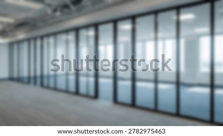 An empty, modern office interior featuring large glass walls, allowing natural light to flood the space. The minimalist design emphasizes clean lines and a sense of openness.