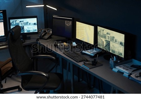 Empty modern office workspace featuring multiple computer monitors displaying surveillance footage, keyboard, mouse, telephone, coffee cup, and office supplies on desk