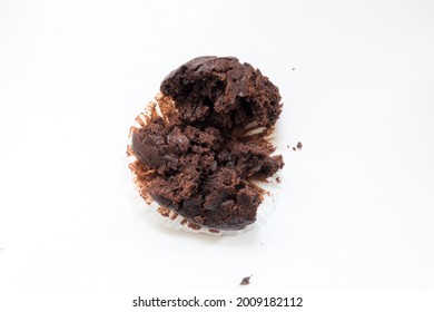 Empty Muffin Wrapper With Half Eaten Chocolate Muffin And Crumbs. Top Down View Of Mess Against A White Background.