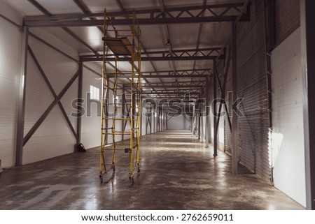 Empty new hangar with windows view from the inside. On the shiny floor under the rays of the sun stand tall construction prefabricated scaffoldingyellow. High quality photo