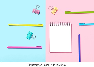 Empty Notebook or notepad on blue and pink background. Various pens. Creative minimalism chancery concept. Top view, flat lay.