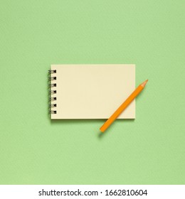 Empty notepad with colored pencil on pastel green background. top view, copy space