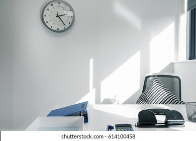 Empty Office Desk And Chair With A Clock Above Emphasising Lateness