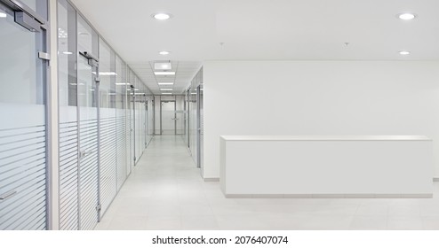 Empty office hall with glass walls and doors. Reception desk and corridor.