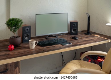 Empty office with large desktop computer monitor, speakers and bonsai on a wooden desk with mobile phone