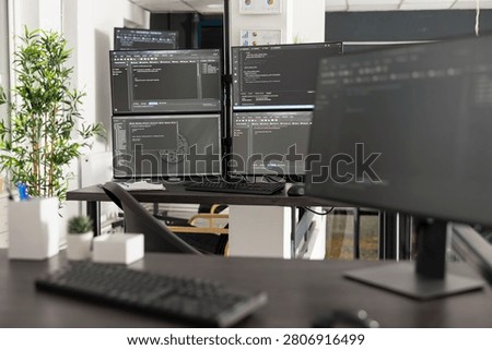 Empty office shows multiple computer screens filled with programming syntax and algorithms, professional workspace represents web development, cybersecurity and digital business solutions.