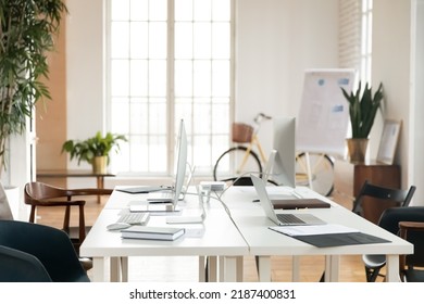 Empty Office Space For Small Team Working Together At Table With Laptops And Computers. Meeting Room With Shared Desk, Workplaces And Houseplants. Modern Business Loft Interior With No People.