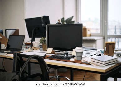 Empty office workspace showing computer monitor, keyboard, reusable coffee cup, scattered documents and supplies on desk, cleaning context implied by absence of people and organized clutter