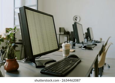 Empty office workspace showing multiple desktops with keyboards and coffee cups. Background including potted plants and office equipment creating professional atmosphere