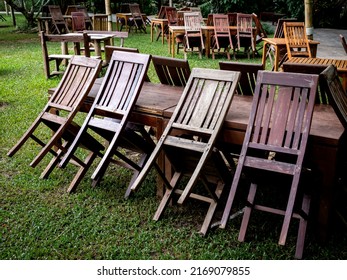 Empty Old Abandoned Wooden Dining Table Set On The Green Yard Garden. Outdoor Restaurant Permanently Closed With Old Dining Table No Use.