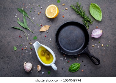 Empty old cast iron skille on dark stone background. Ingredients for making steak  concept with copy space . Various herbs and seasoning rosemary ,sage ,bay leaves ,basil ,garlic and peppercorn.