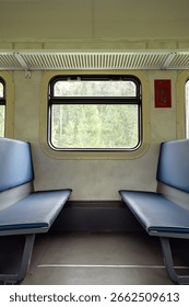 Empty old train compartment interior with blue seats and outside green nature through the window.