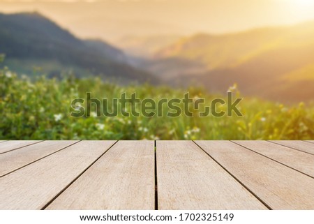 Empty old wooden table in front of blurred view on top of mountains and green field with beautiful sunset background of nature. Can be used for display or montage for show your products.