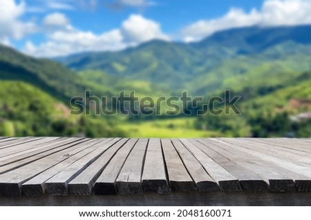Empty old wooden table in front of blurred beautiful organic rice field, mountain, forest and cloud on blue sky at country side on clear day. Can be used for display or montage for show your product.